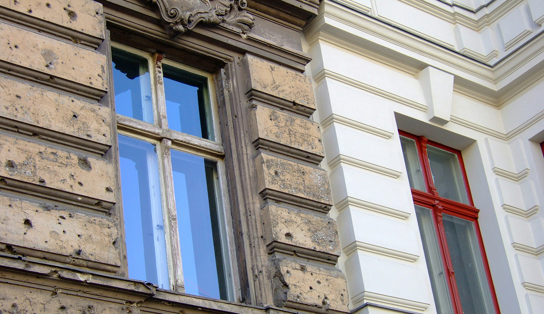 Fassadenansicht eines Altbaus in Wien – rechts renoviert, links mit sichtbaren Bauschäden wie Rissen und Abplatzungen